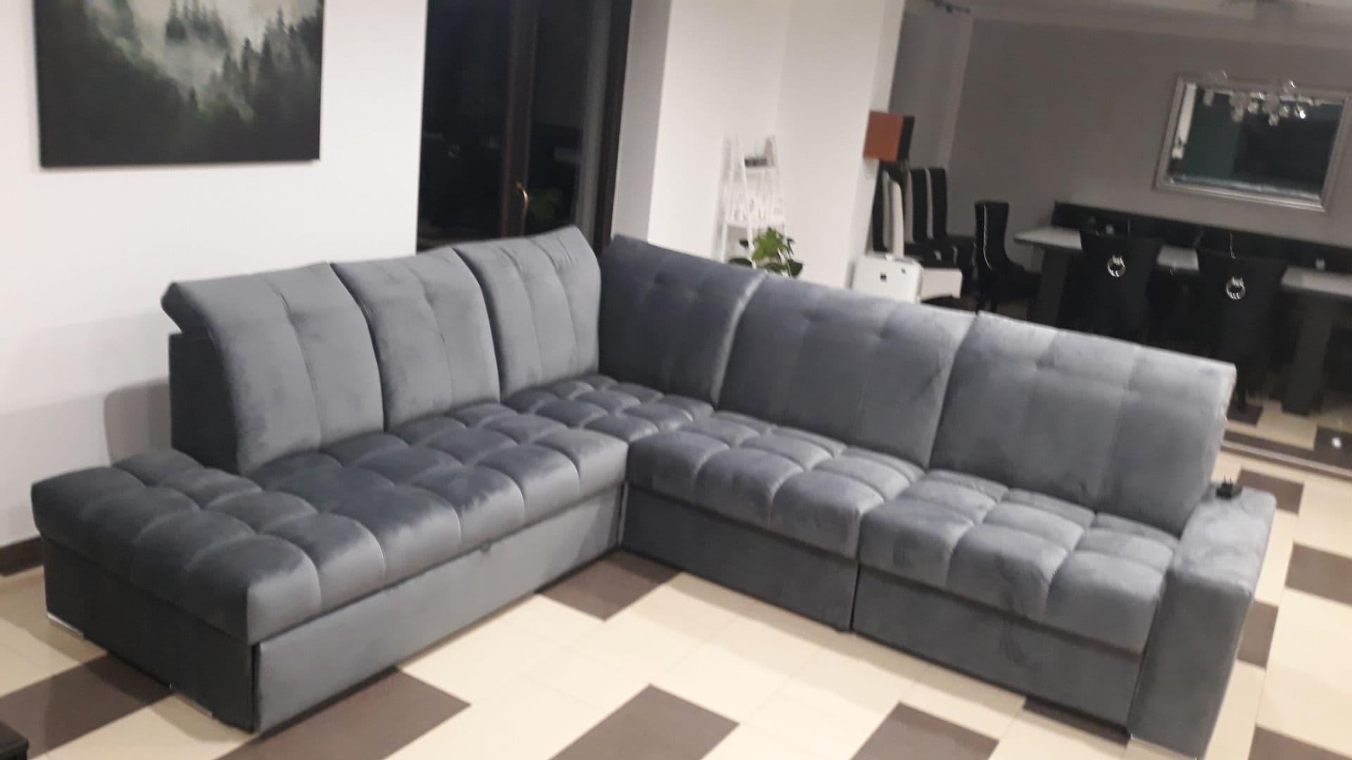 Szary, narożny, tapicerowany zestaw wypoczynkowy z pikowanymi siedziskami w salonie z obrazem na ścianie i czarnym stołem z krzesłami w tle.