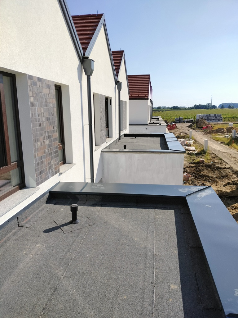 Nowe, płaskie dachy pokryte papą termozgrzewalną z obróbkami blacharskimi na szeregu domów jednorodzinnych w trakcie budowy.