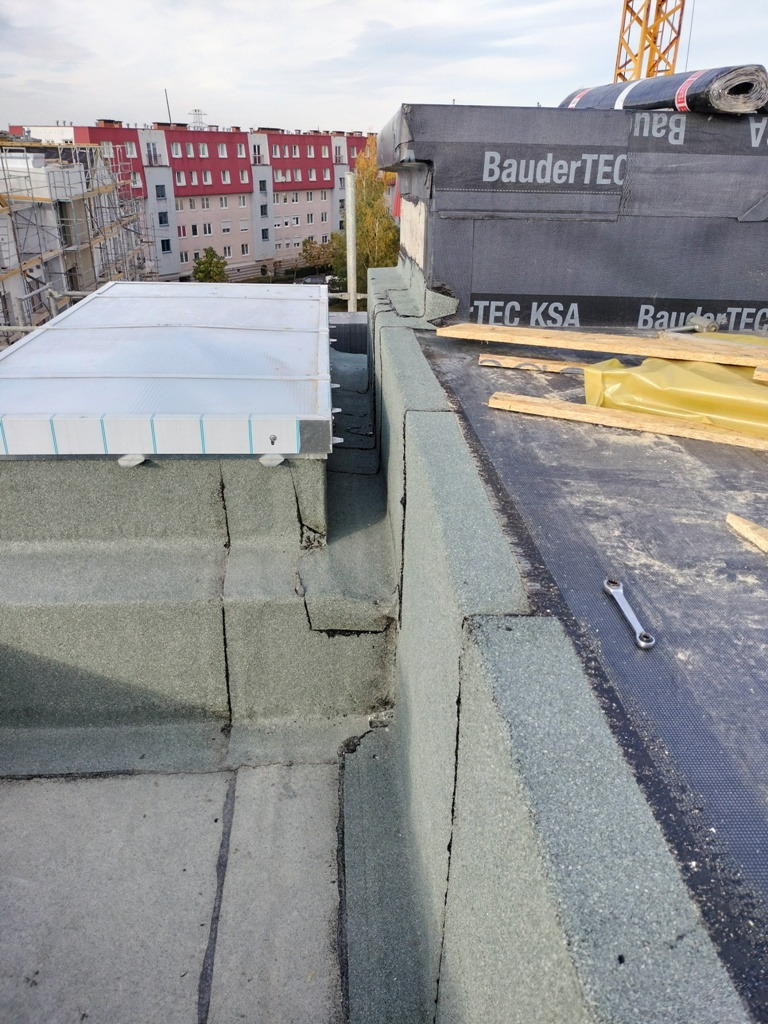 Wykończenie dachu płaskiego z papy termozgrzewalnej, widoczny świetlik dachowy, obróbka blacharska i narzędzie - klucz płaski.