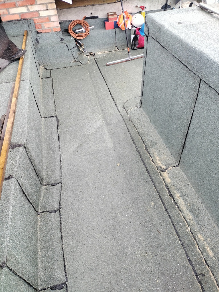 Płaski dach pokryty papą termozgrzewalną z obróbkami blacharskimi, narzędzia i materiały dekarskie w tle, widoczne łączenia papy.