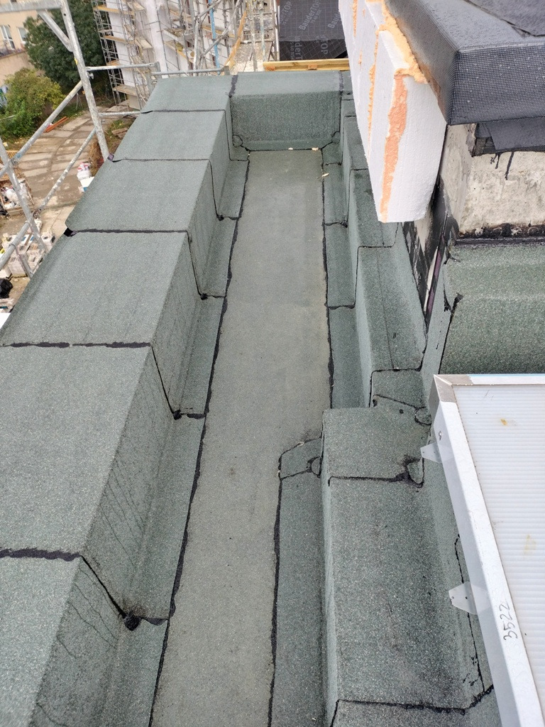 Szczegółowe ujęcie dachu z papy w Kiełczowie, ukazujące obróbki blacharskie i izolację termiczną styropianem, widoczne elementy konstrukcyjne i uszczelnienia.