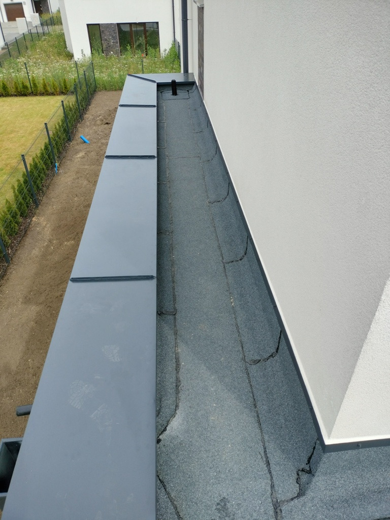 Nowoczesny dach płaski z obróbką blacharską w kolorze grafitowym, widok z góry, zarys budynku w tle.