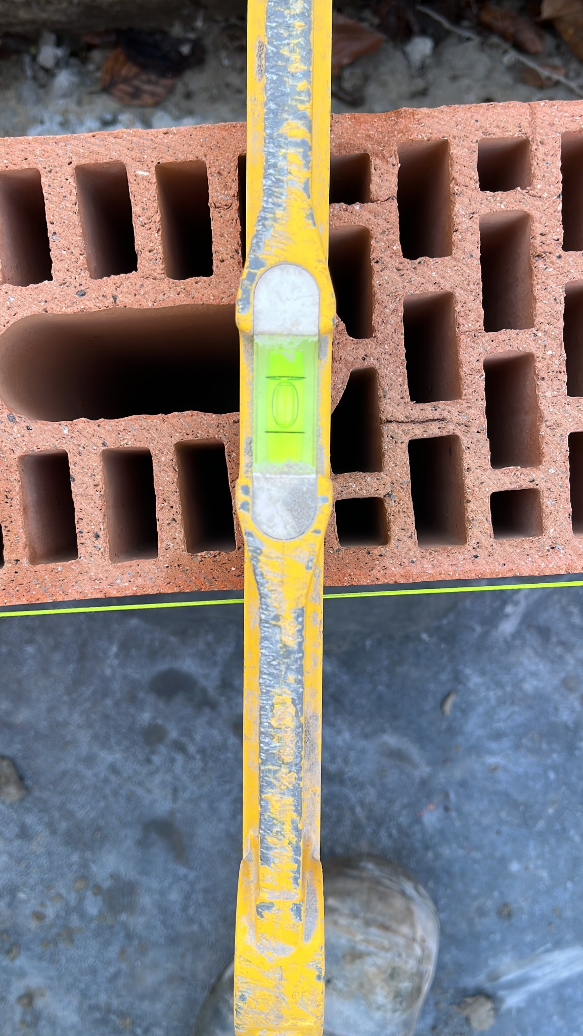Żółta poziomica murarska ustawiona na bloczku ceramicznym z widoczną zieloną libellą wskazującą poziom.