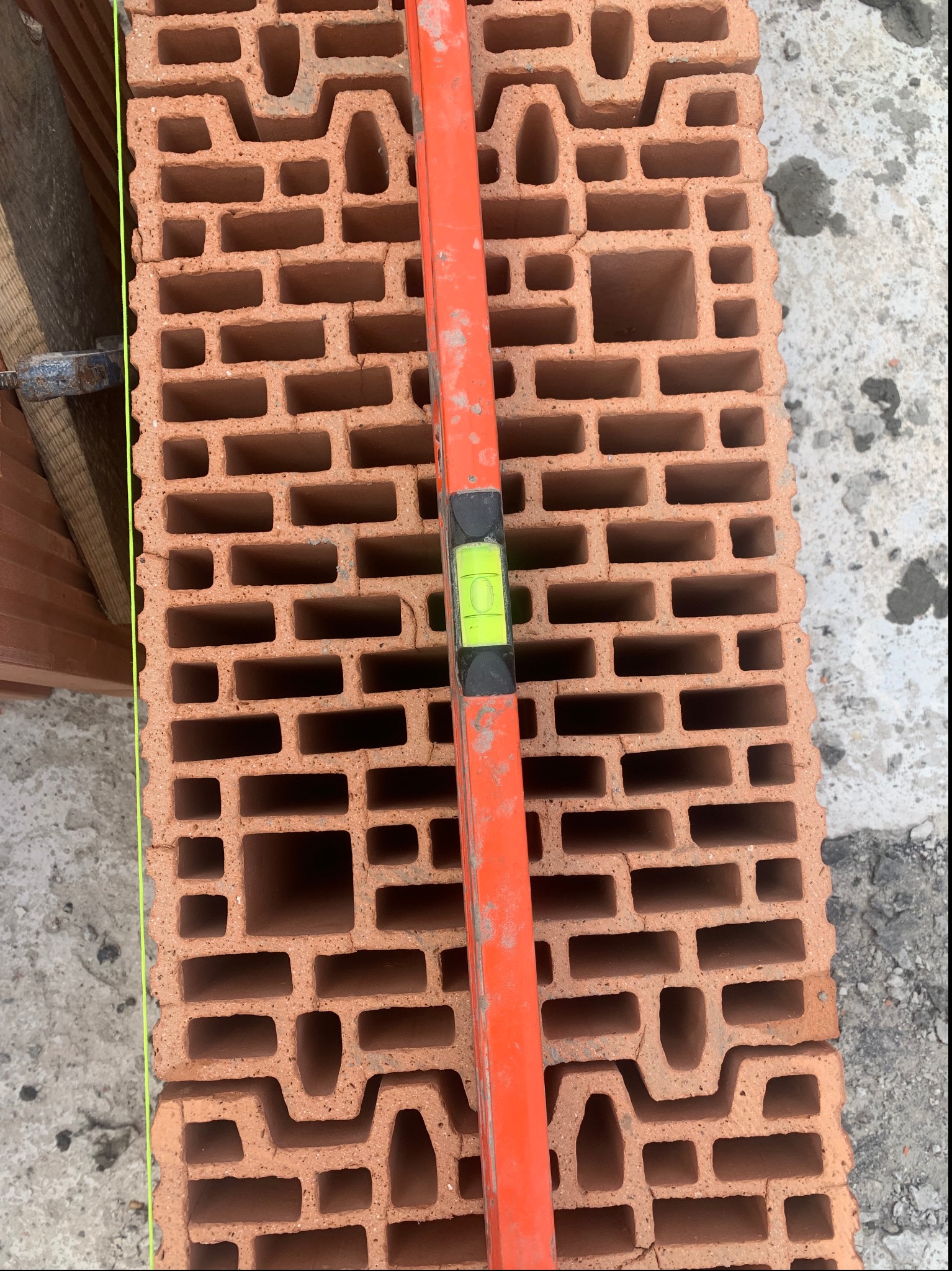 Cegła ceramiczna Porotherm z poziomnicą w pionie, widoczne puste przestrzenie w cegle, ślad zaprawy po lewej stronie.