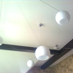 budobel.pl - Biały sufit z zamontowanymi kulistymi lampami wiszącymi na cienkich linkach i dekoracyjnymi, ciemnobrązowymi belkami