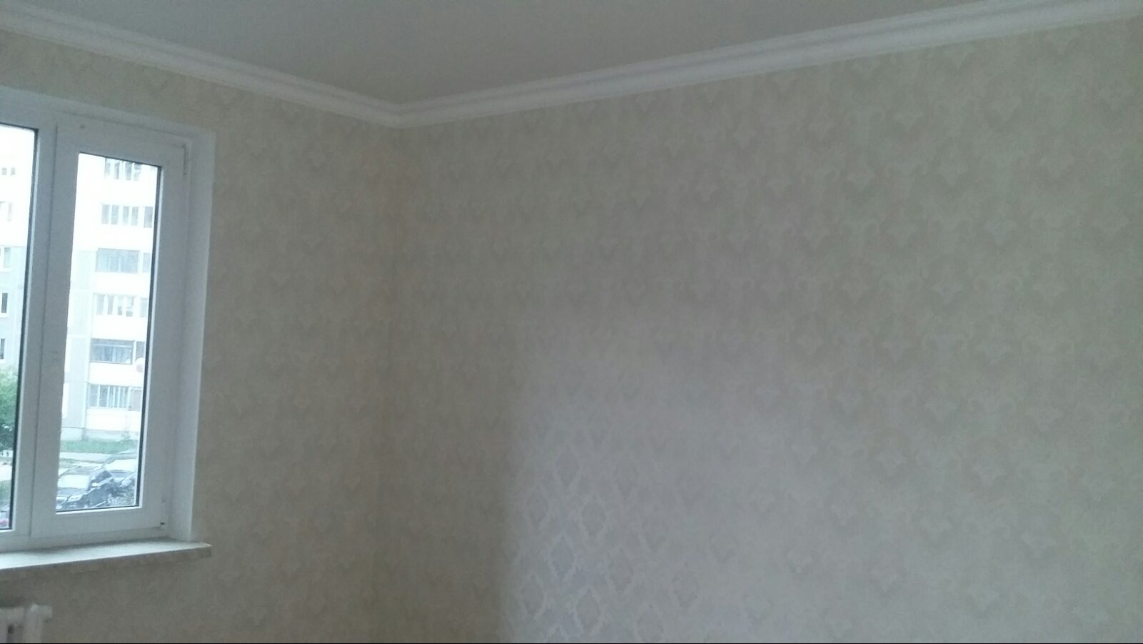 Ściana po malowaniu z delikatnym wzorem, widoczna biała listwa przysufitowa i okno PCV z widokiem na blok.