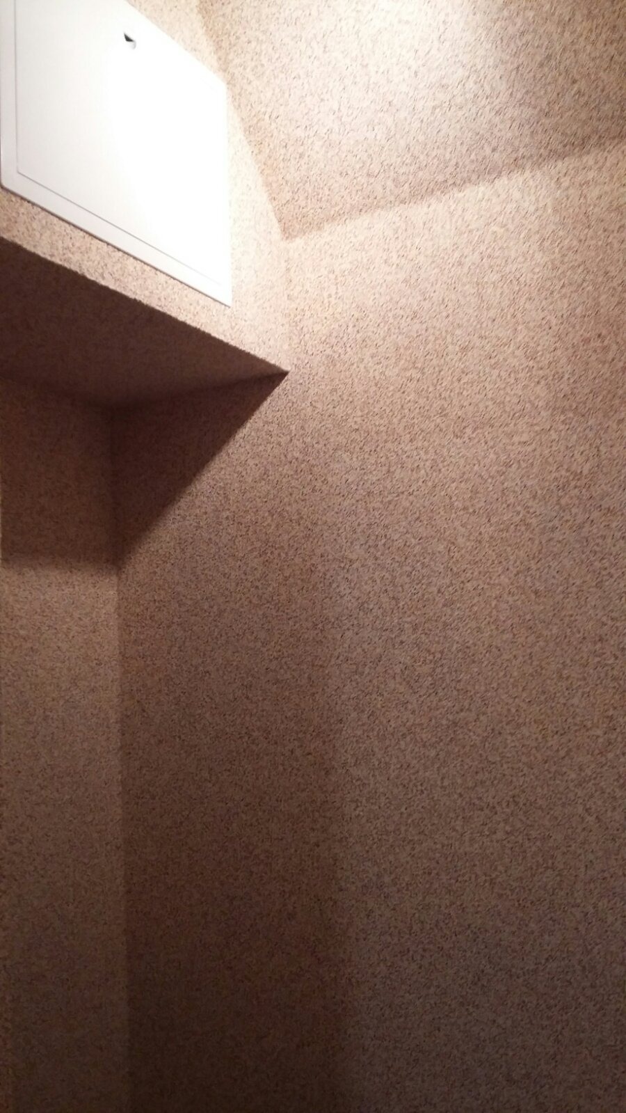 Fragment wnętrza z beżową, teksturowaną ścianą, białą klapą rewizyjną i wnęką.