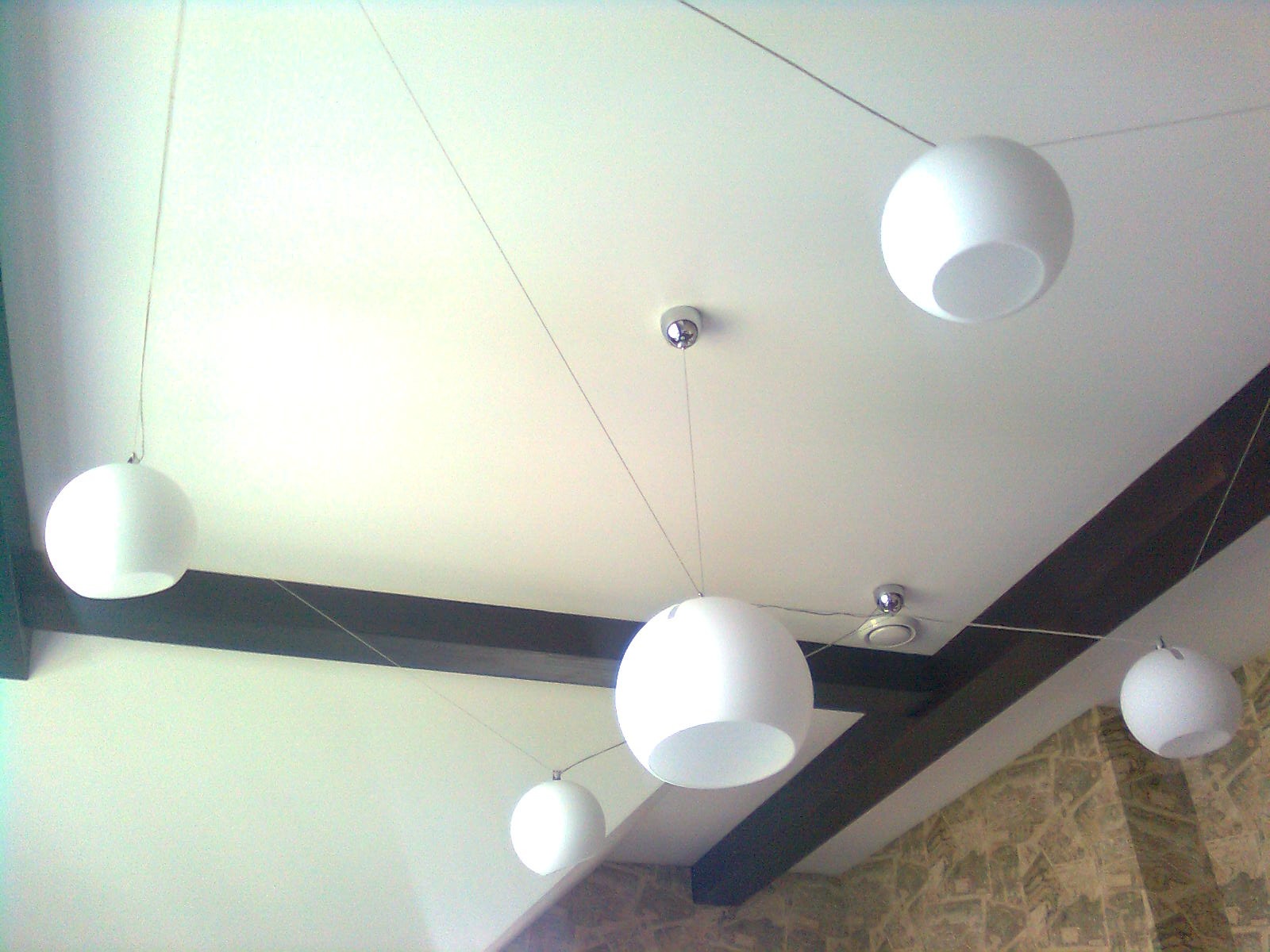 Biały sufit z zamontowanymi kulistymi lampami wiszącymi na cienkich linkach i dekoracyjnymi, ciemnobrązowymi belkami