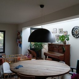 Malmaster - Jasne wnętrze domu z drewnianym stołem, czarną lampą wiszącą, pianinem i dekoracjami.