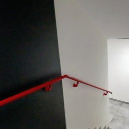 Malmaster - Klatka schodowa po remoncie: czarna ściana kontrastuje z białą, a czerwona poręcz dodaje akcentu kolorystycznego. Widoczne płytki na podłodze i świeżo pomalowane ściany.