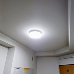 Malmaster - Białe wnętrze korytarza z okrągłą lampą sufitową, widoczne drzwi z numerem 46 i szafka elektryczna. Świeżo pomalowane ściany w neutralnym odcieniu bieli.