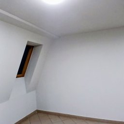 Malmaster - Wnętrze pokoju po remoncie w Rościsławicach. Białe ściany, beżowa podłoga z płytek, skośne okno dachowe i okrągła lampa sufitowa.