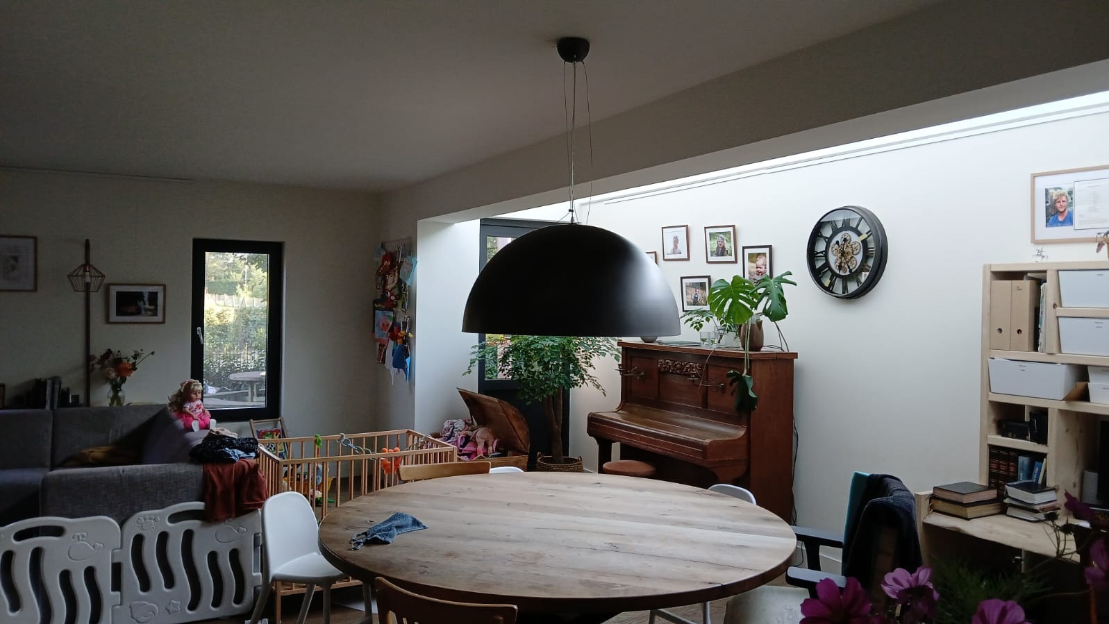 Jasne wnętrze domu z drewnianym stołem, czarną lampą wiszącą, pianinem i dekoracjami.