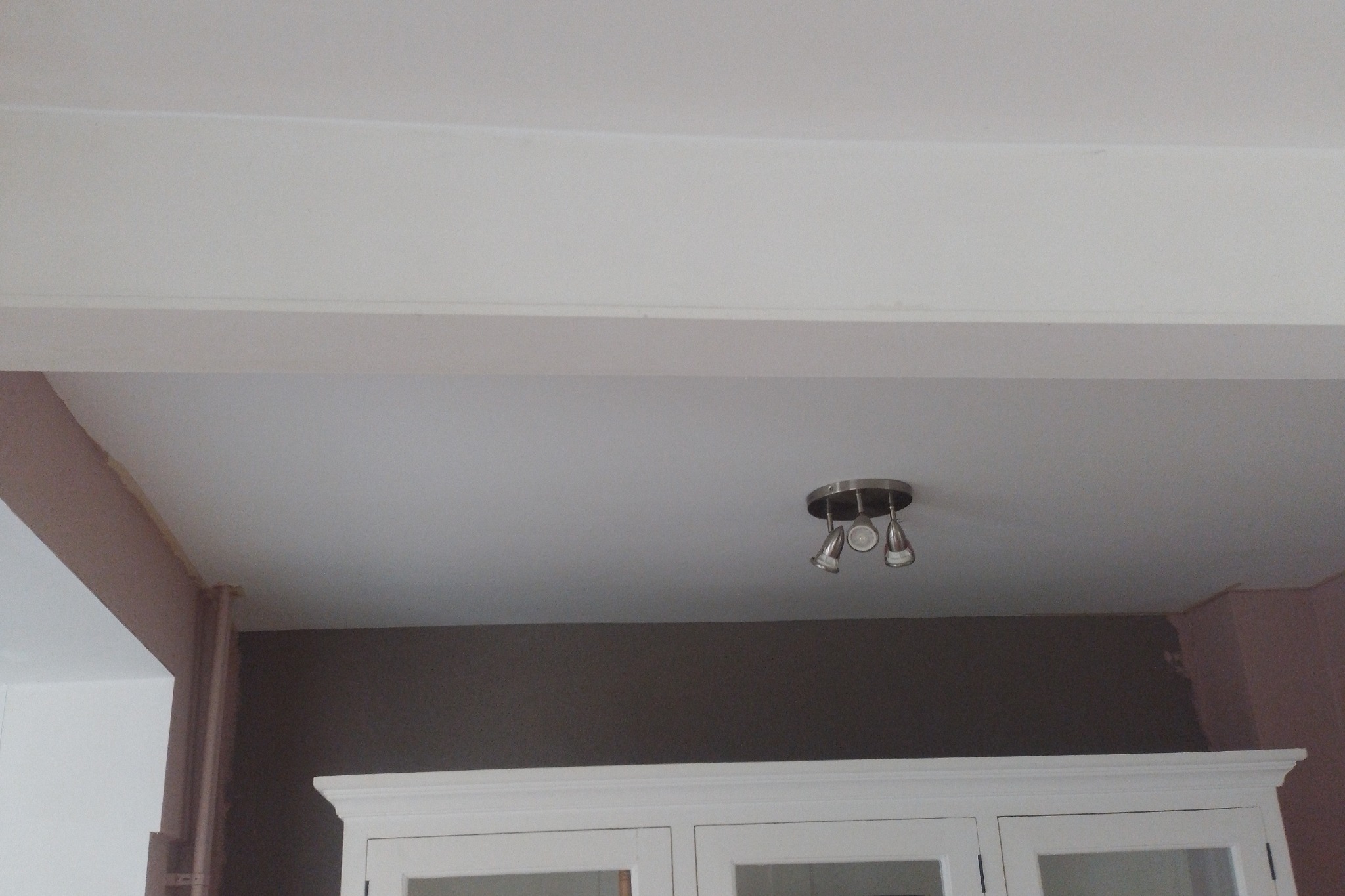 Wnętrze w trakcie odświeżania: fragment sufitu z lampą punktową, ściana w dwóch kolorach, widoczne ślady szpachlowania na ścianie i suficie.