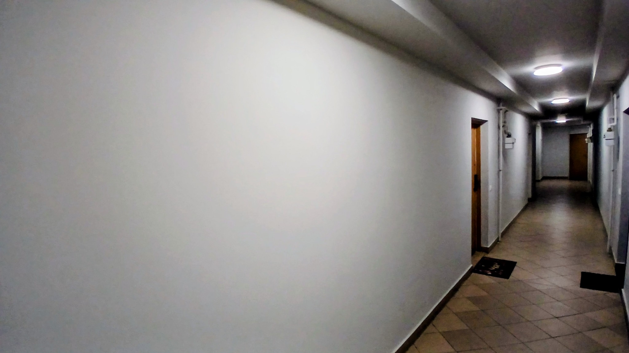 Korytarz w budynku wielorodzinnym po odświeżeniu ścian, widoczne drzwi i płytki podłogowe. Ściany pomalowane na jasny kolor, oświetlenie sufitowe.