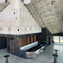 Andrii Pominchuk - Wnętrze nowoczesnego baru z surowym betonowym sufitem, podwieszanymi lampami, dekoracyjną ścianą z podświetleniem i osobą w tle.