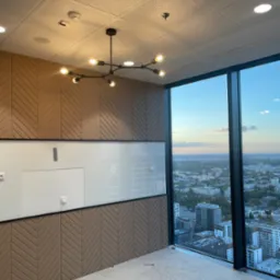 Nowoczesne biuro z panoramicznym widokiem na miasto, designerska lampa sufitowa z żarówkami Edisona, dekoracyjna ściana z panelami w jodełkę i biała tablica suchościeralna.