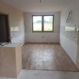 Układanie drewnopodobnych płytek podłogowych w kuchni w Kosowie Lackim, widoczne narzędzia na blacie i częściowo wykończone ściany z marmurowymi płytkami.