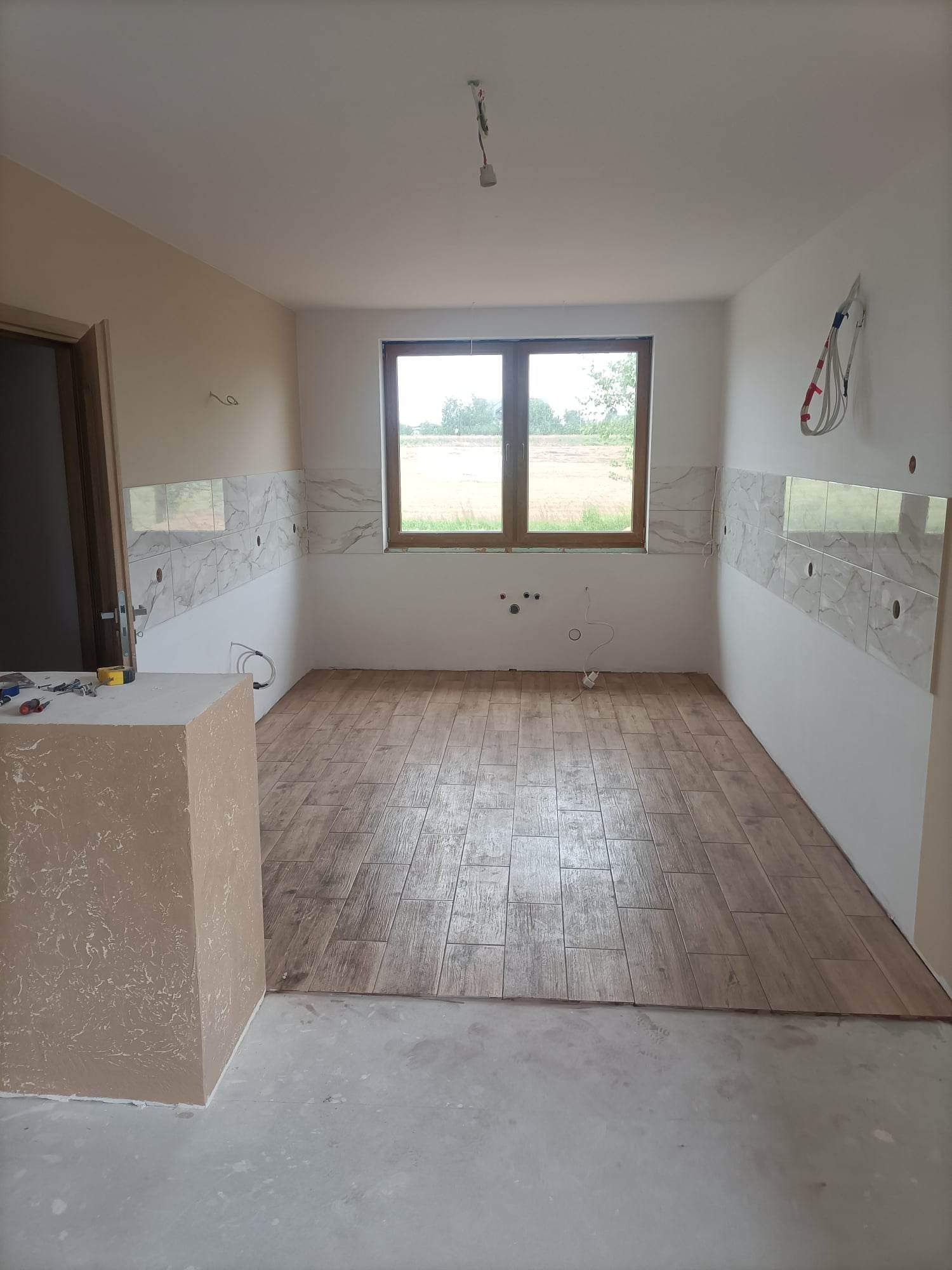 Układanie drewnopodobnych płytek podłogowych w kuchni w Kosowie Lackim, widoczne narzędzia na blacie i częściowo wykończone ściany z marmurowymi płytkami.