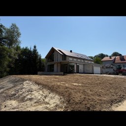 PROJAR - Surowy dom z betonu komórkowego w trakcie budowy, z widoczną koparką w tle i przygotowanym terenem. Ukazany w słoneczny dzień.