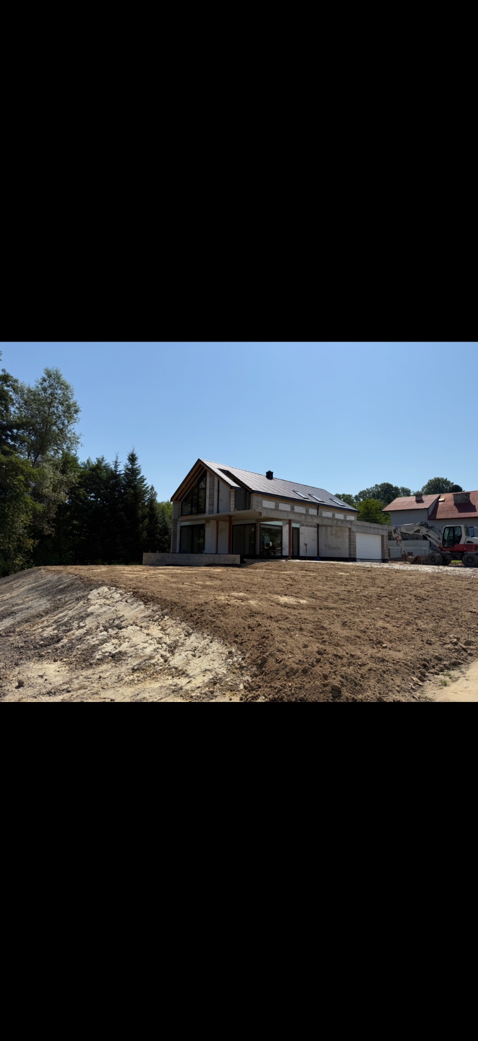 Surowy dom z betonu komórkowego w trakcie budowy, z widoczną koparką w tle i przygotowanym terenem. Ukazany w słoneczny dzień.