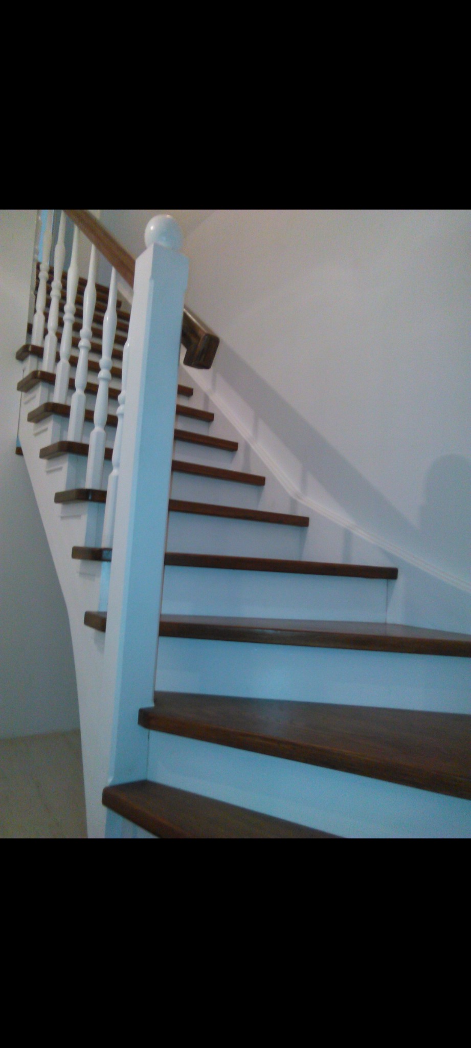 Nowoczesne schody wewnętrzne z drewnianymi stopniami w kolorze ciemnego orzecha i białymi balustradami z ozdobnymi tralkami.