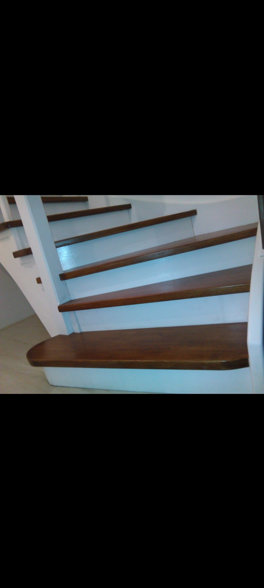 Białe schody z drewnianymi stopniami o zaokrąglonych krawędziach, widok od dołu.