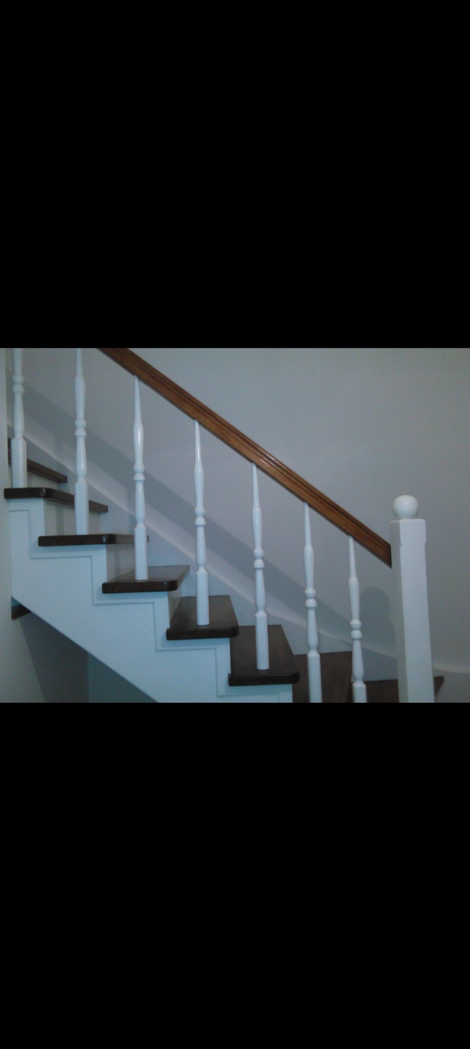 Klasyczne schody z drewnianymi stopniami w ciemnym odcieniu, białą balustradą z toczonymi tralkami i drewnianą poręczą, widoczne z dołu.