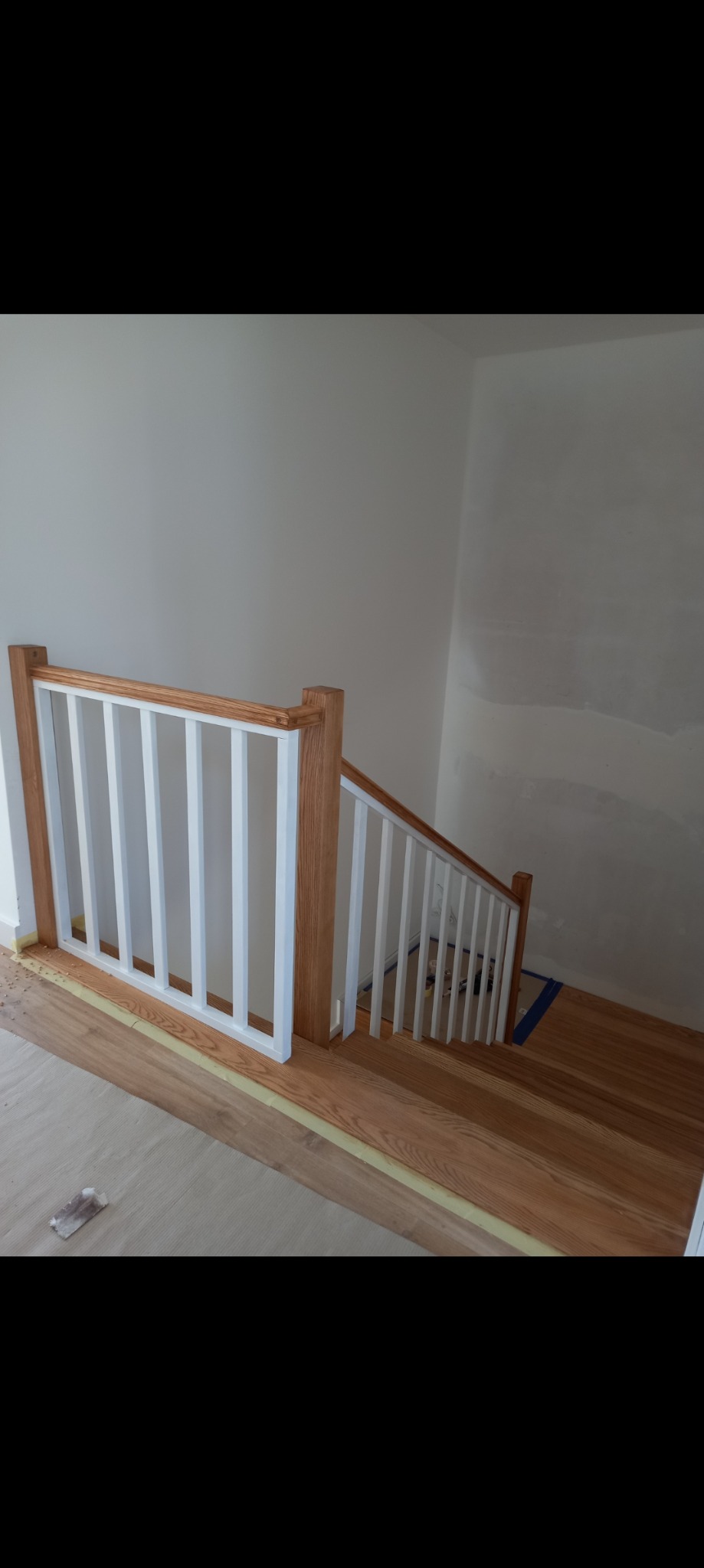 Drewniane schody z białą balustradą w trakcie montażu, zabezpieczone taśmą malarską, widoczne niedomalowane ściany.