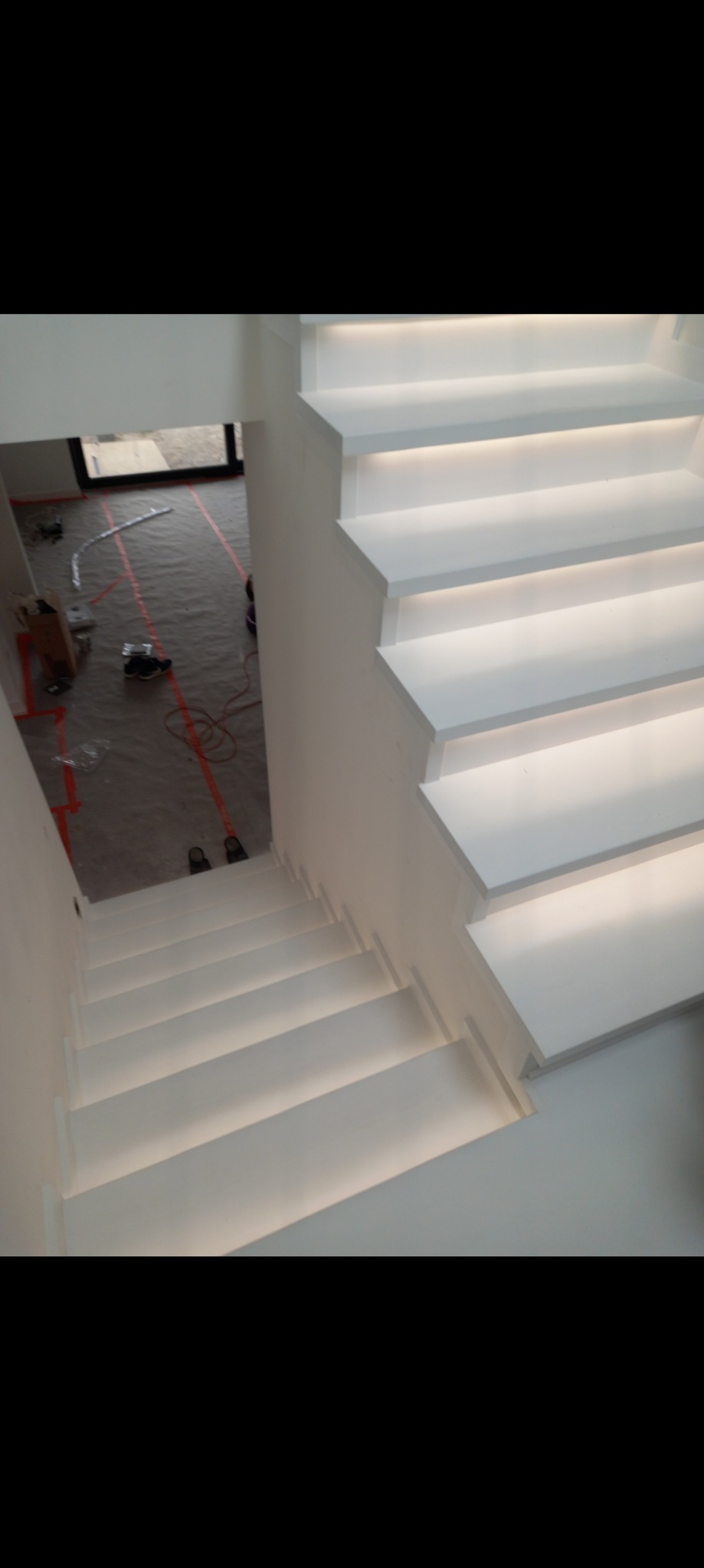 Nowoczesne, białe schody z podświetleniem LED, widok z góry na korytarz w trakcie remontu, zabezpieczona podłoga.