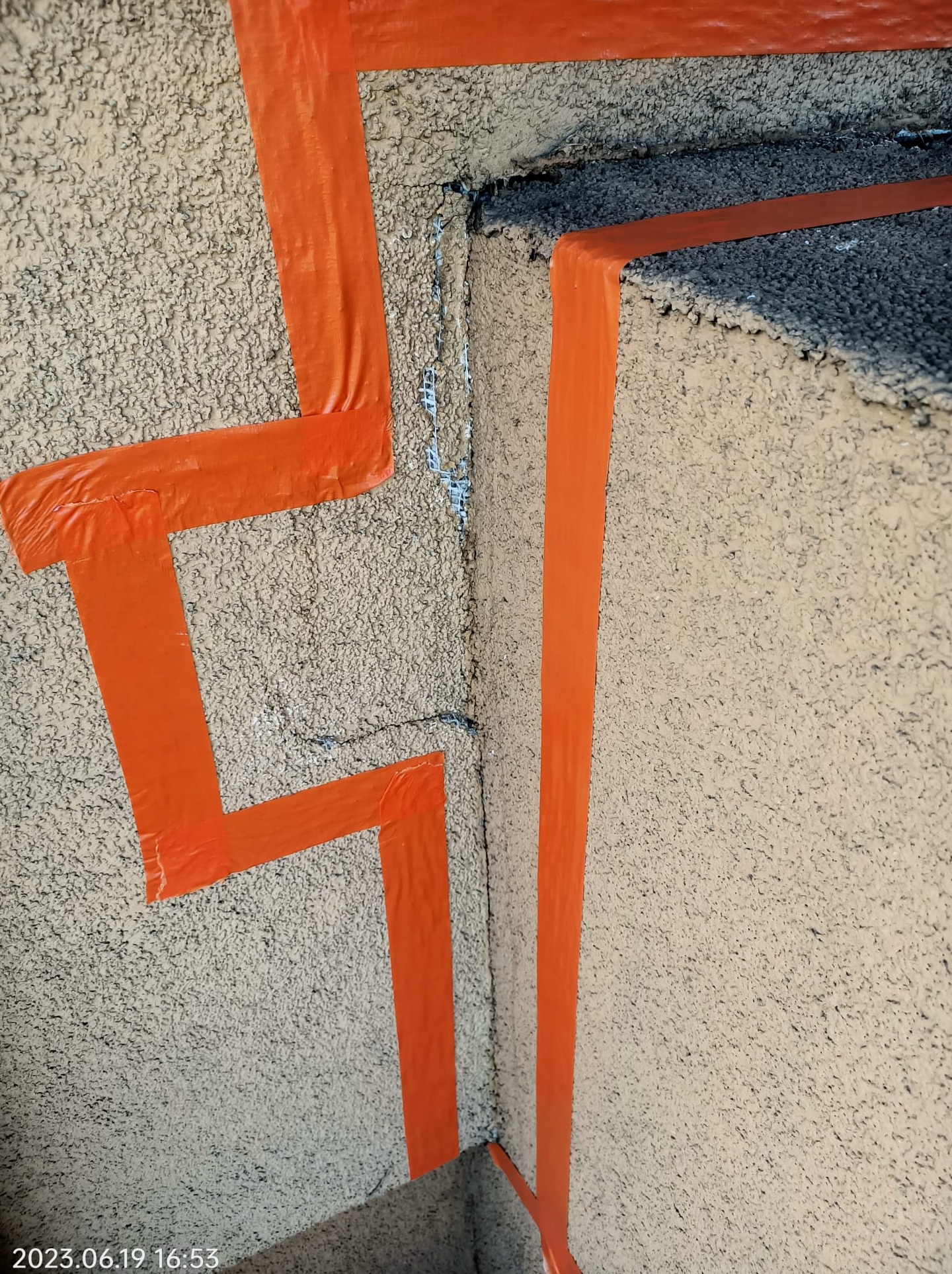 Przygotowanie elewacji do malowania: pomarańczowa taśma malarska wyznacza granice na chropowatej powierzchni ściany.