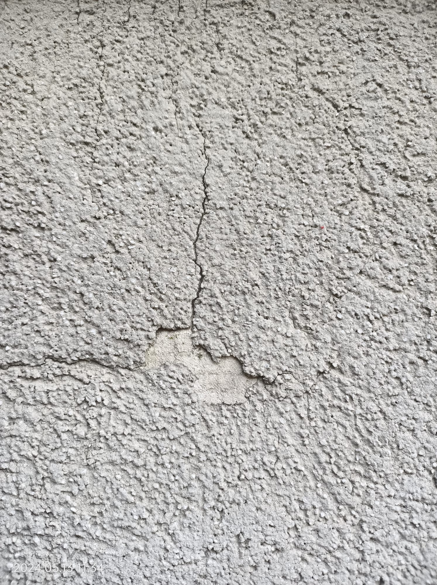 Szara, ziarnista elewacja z widocznym pęknięciem i ubytkiem odsłaniającym jaśniejszą warstwę pod spodem.