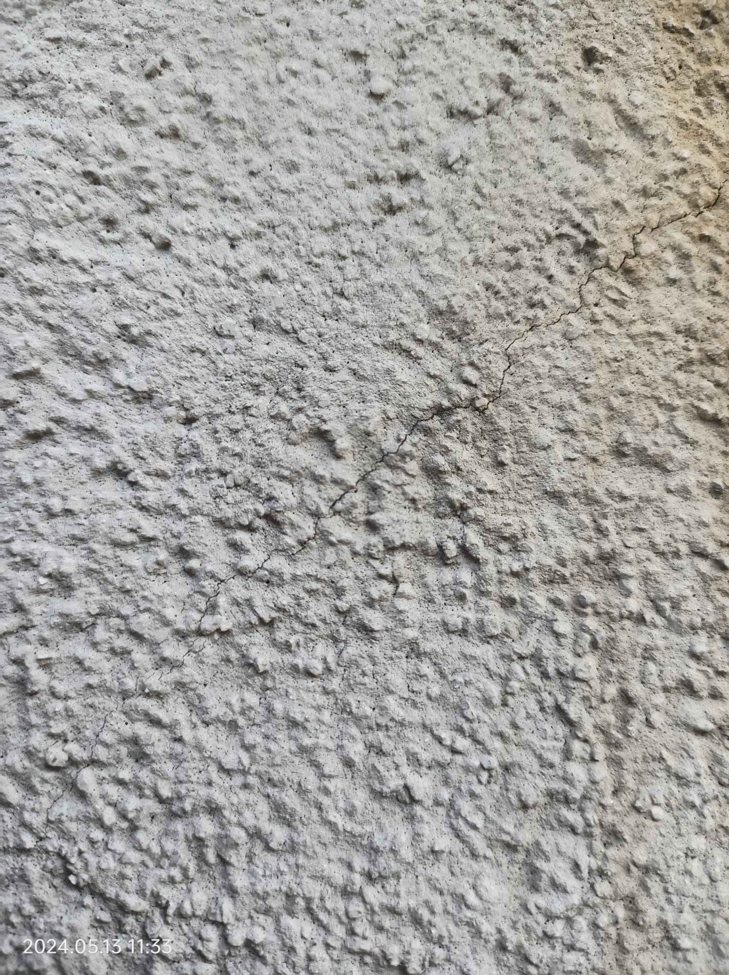 Szara, chropowata elewacja z widocznymi drobnymi pęknięciami, oświetlona naturalnym światłem.