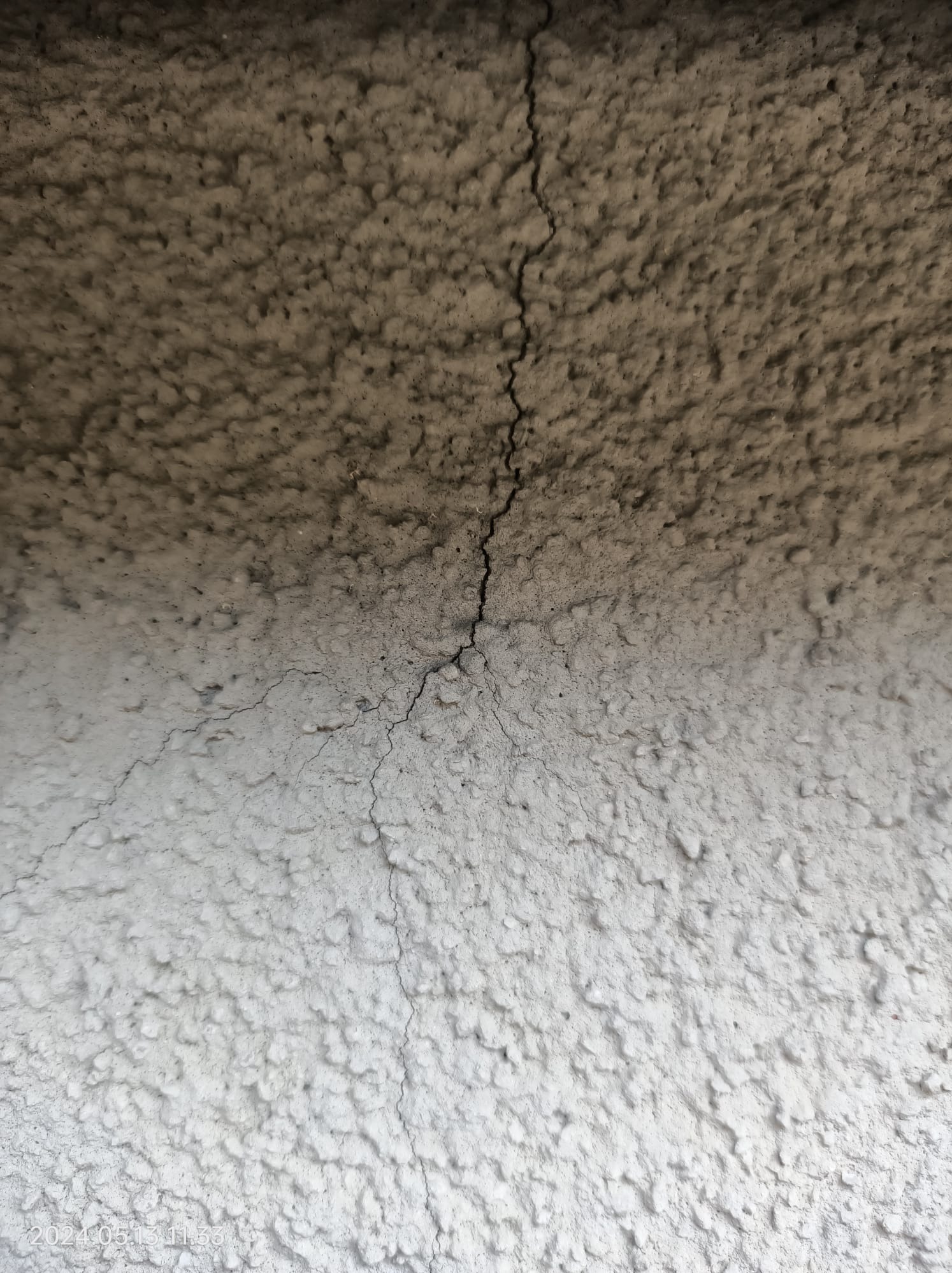 Pęknięcie na szpachlowanej ścianie w Cieszynie, widoczna wyraźna linia pęknięcia biegnąca pionowo przez strukturę.