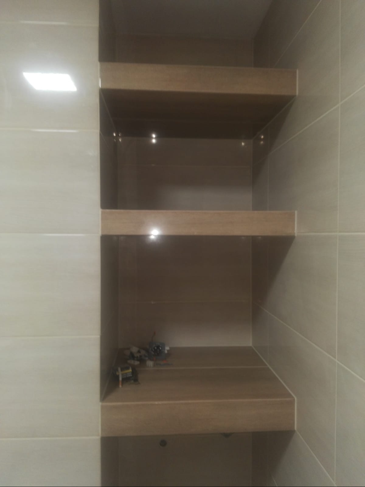 Wnęka z półkami wykończona płytkami ceramicznymi w odcieniach beżu i brązu, na dolnej półce leżą zabawki Lego.