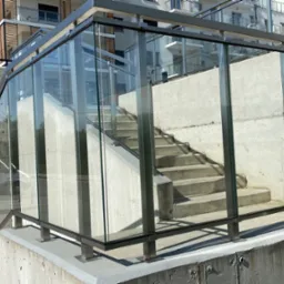 Zewnętrzne schody betonowe z przeszkloną balustradą w Rzeszowie, widoczne z poziomu chodnika, z budynkiem w tle.