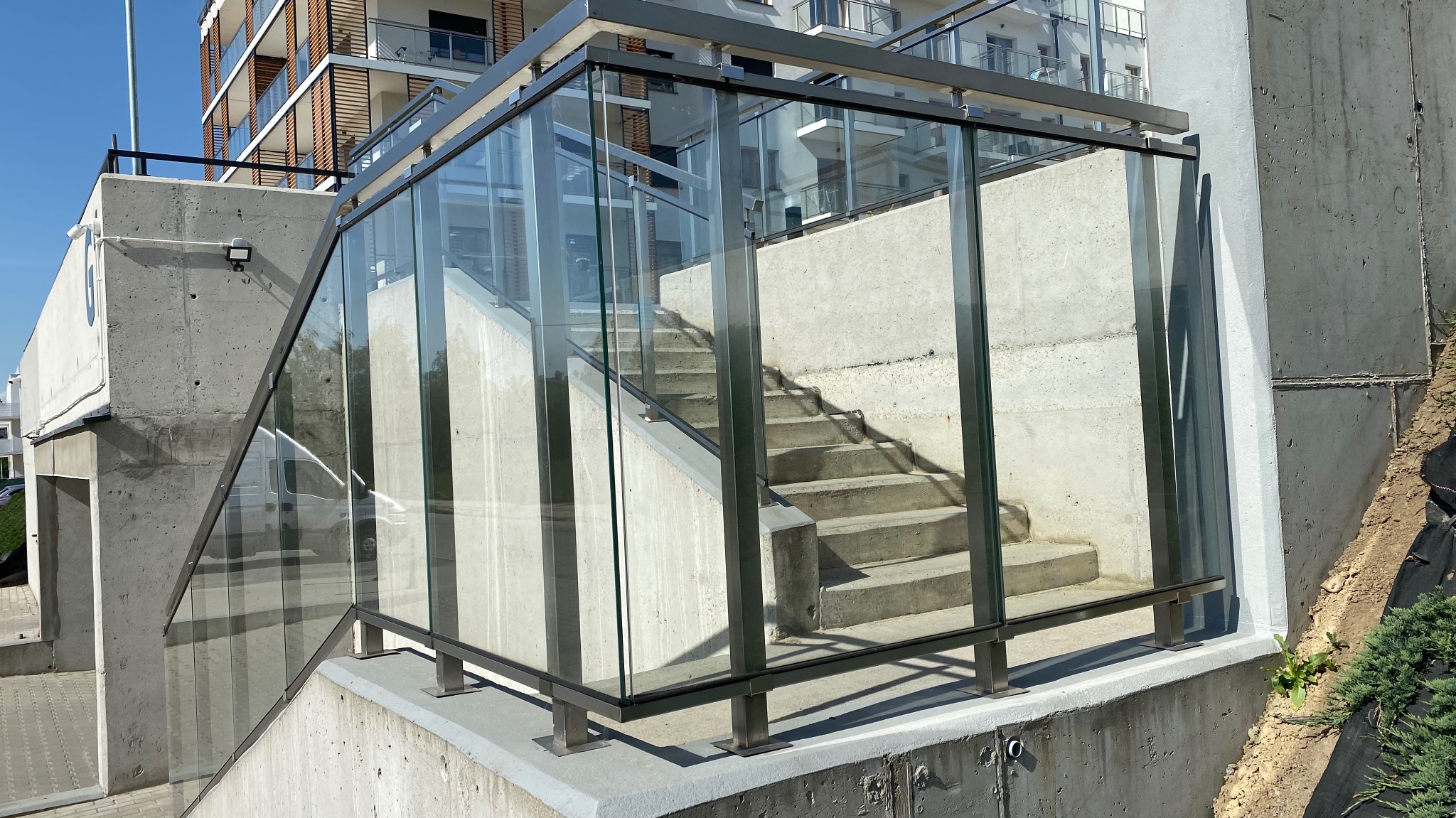 Zewnętrzne schody betonowe z przeszkloną balustradą w Rzeszowie, widoczne z poziomu chodnika, z budynkiem w tle.