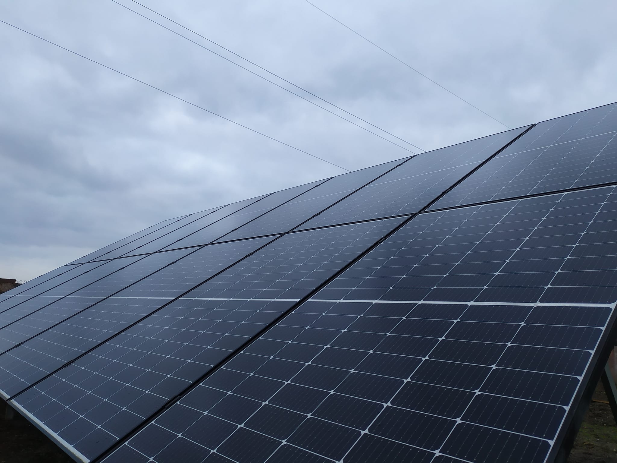 Panel słoneczny ustawiony pod kątem na tle pochmurnego nieba z widocznymi liniami energetycznymi w oddali.
