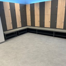 Patrycja Sutryk Czysty Kącik - Wnętrze szatni z rzędem zamykanych szafek w kolorach drewna i grafitu, oraz szarą ławką z metalową konstrukcją.