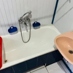 Wanna z czerwonym ociekaczem na akcesoria, różową umywalką i chromowaną baterią, widoczne niebieskie mydelniczki, białe panele ścienne z niebieskimi akcentami.