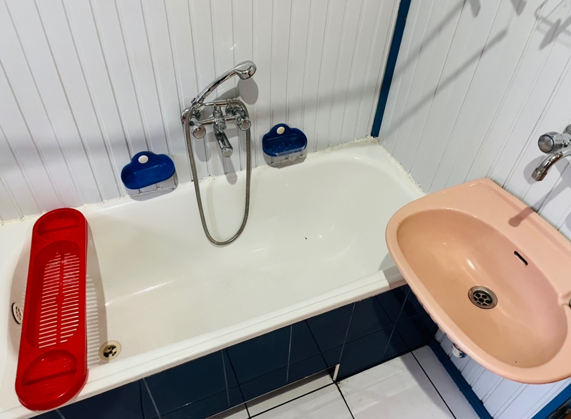 Wanna z czerwonym ociekaczem na akcesoria, różową umywalką i chromowaną baterią, widoczne niebieskie mydelniczki, białe panele ścienne z niebieskimi akcentami.
