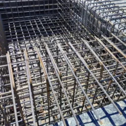 Zbrojenie stalowe w wykopie fundamentowym, przygotowane do zalania betonem, widoczne pręty pionowe i poziome tworzące siatkę, folia izolacyjna pod spodem.