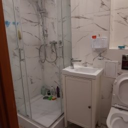 Masters Gres Jan Zonenberg - Wykończona łazienka z kabiną prysznicową, umywalką z szafką i toaletą, wyłożona płytkami imitującymi marmur i wzorzystymi heksagonami na podłodze.