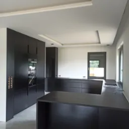 Nowoczesna kuchnia w kolorze antracytowym z wyspą kuchenną i zabudową pod sufit, minimalistyczne uchwyty, szare płytki podłogowe.