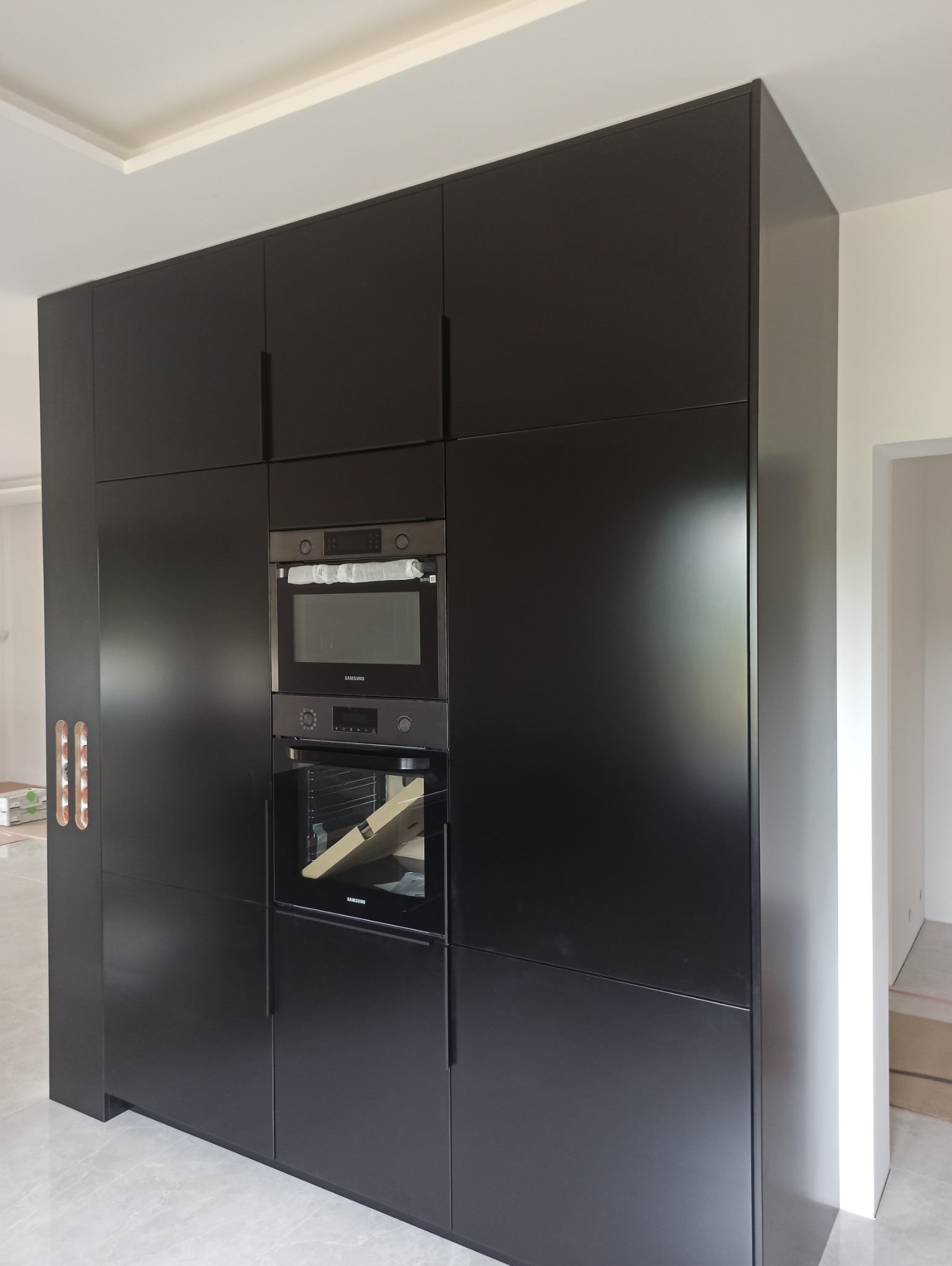 Czarna zabudowa kuchenna z piekarnikiem i mikrofalówką marki Samsung, widoczne uchwyty frezowane w jednych z szafek.