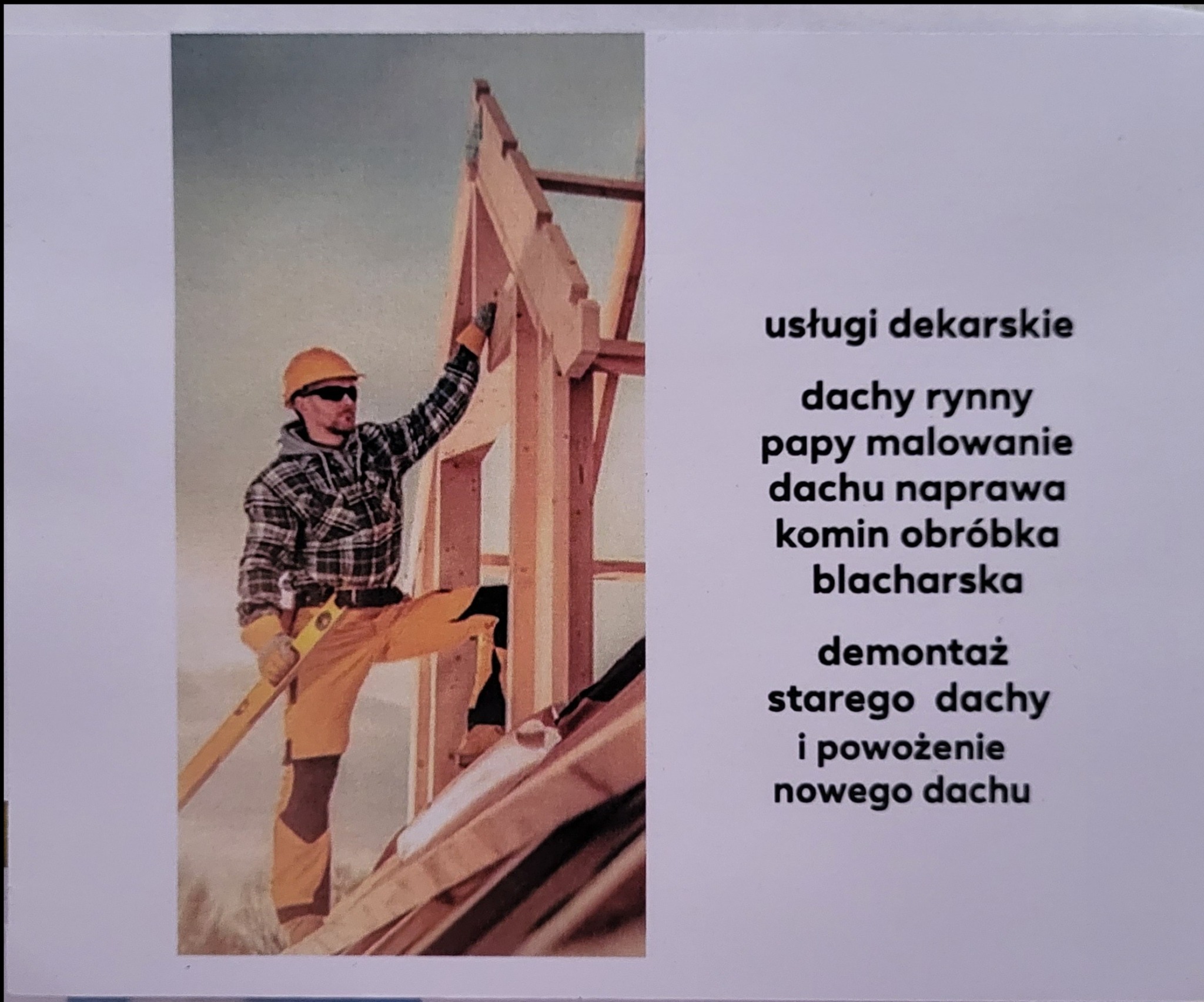 Dekarz w kasku i okularach przeciwsłonecznych, w koszuli w kratę, montuje drewnianą konstrukcję dachu, trzyma poziomicę