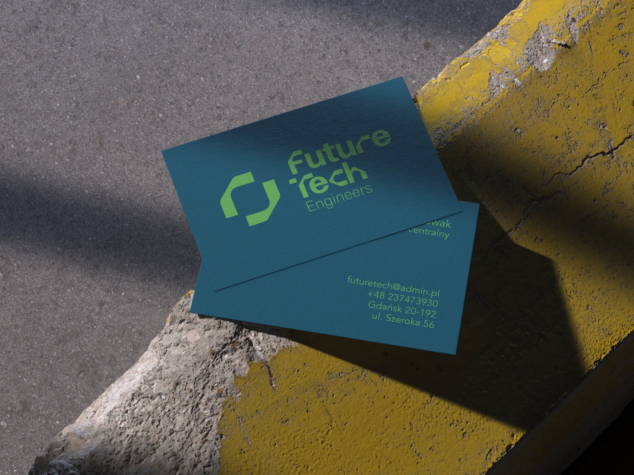 Dwie turkusowe wizytówki z zielonym logo 'Future Tech Engineers' leżące na krawężniku pomalowanym na żółto, rzucające cień.