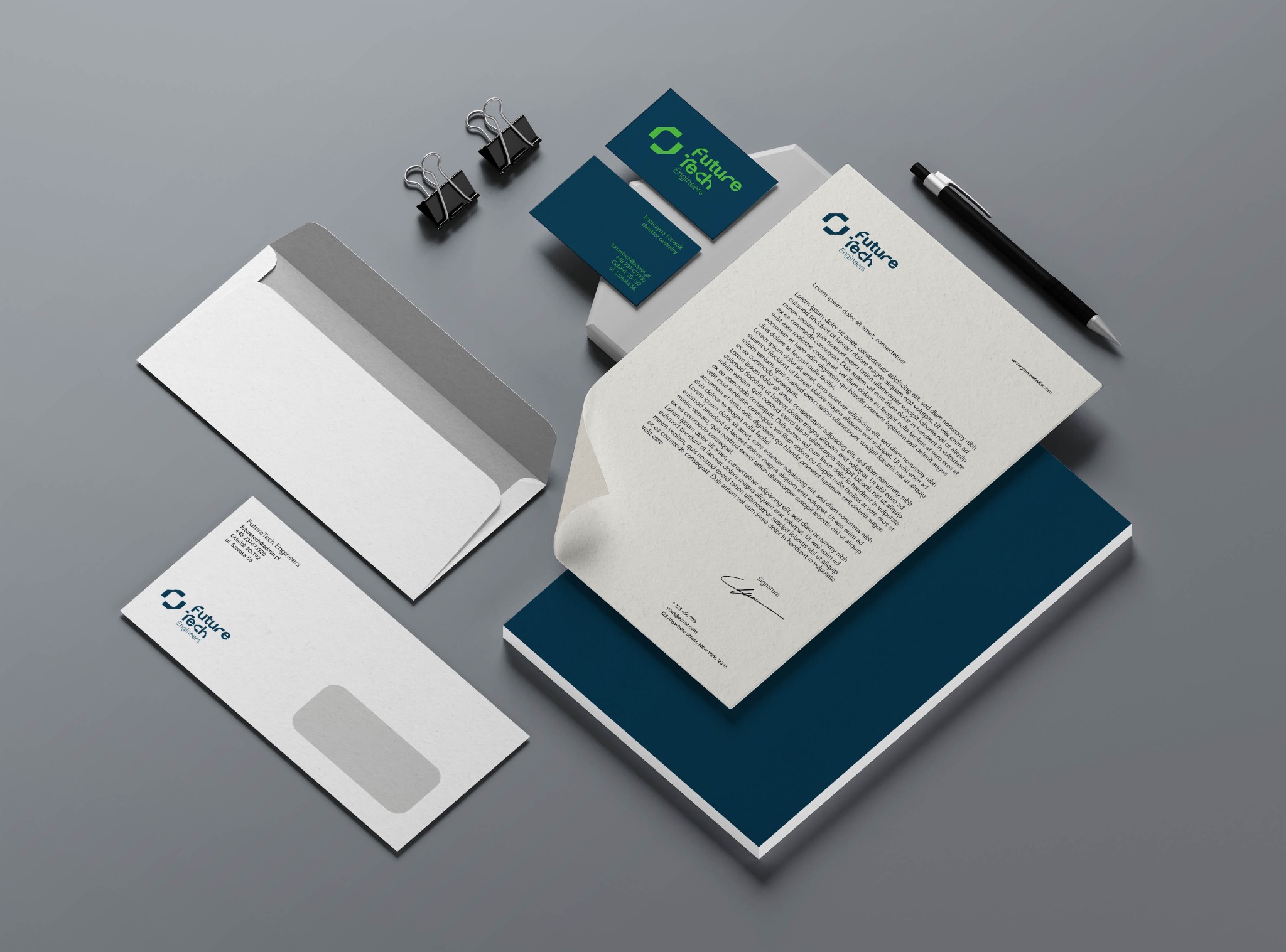 Komplet materiałów firmowych na szarym tle: papier firmowy z logo, wizytówki, koperty DL, czarny długopis i dwa klipsy biurowe.