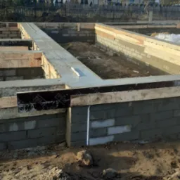 Wylane fundamenty pod budynek z bloczków betonowych, widoczne zbrojenia i poziomica, w tle zabudowa szeregowa.