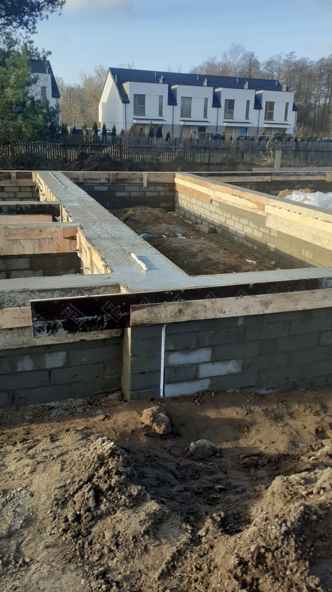 Wylane fundamenty pod budynek z bloczków betonowych, widoczne zbrojenia i poziomica, w tle zabudowa szeregowa.